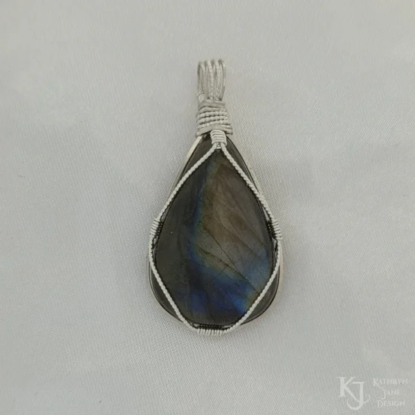 Photo taken in a filter cone to eliminate appearance of reflections off the surface Triangular-shaped natural labradorite pendant in a simple sterling silver framework on white satin background.