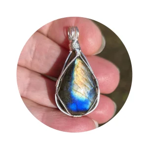 Triangular-shaped natural labradorite pendant in a simple sterling silver framework in hand in bright sunlight. Labradorescence showing brilliant gold and electric blue