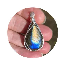Triangular-shaped natural labradorite pendant in a simple sterling silver framework in hand in bright sunlight. Labradorescence showing brilliant gold and electric blue