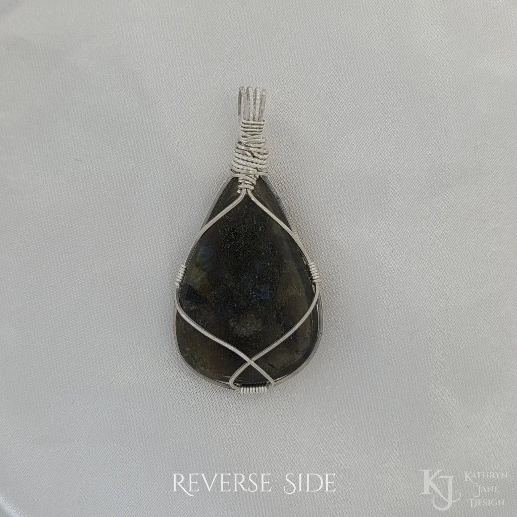 Reverse side of triangular-shaped natural labradorite pendant in a simple sterling silver framework on white satin background.