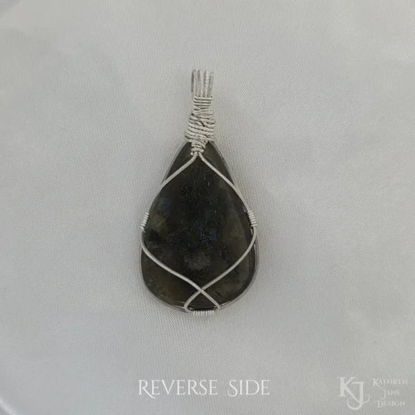 Reverse side taken in filtered light Reverse side of triangular-shaped natural labradorite pendant in a simple sterling silver framework on white satin background.