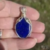 In direct sunlight outdoors Oblong-shaped royal blue lapis lazuli pendant with sterling silver and 14k gold-filled wire spirals at the top, and in the bail. Held in hand in direct sunlight