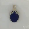 Photo taken in filter cone, eliminating the appearance of reflections off the highly polished surface of the stone Oblong-shaped royal blue lapis lazuli pendant with sterling silver and 14k gold-filled wire spirals at the top, and in the bail. White satin background with Kathryn Jane Design logo in the bottom right