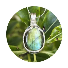 Teal-green and gold oval labradorite pendant with elegant square and twisted sterling silver wire framework against background of green leaves