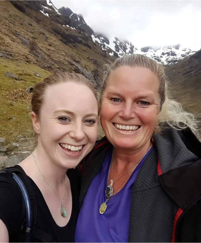 Kathryn visiting her eldest daughter in the Scottish Highlands in 2018. Snow is on the mountains behind. Kathryn's face is tanned. Her daughter's is pale.
