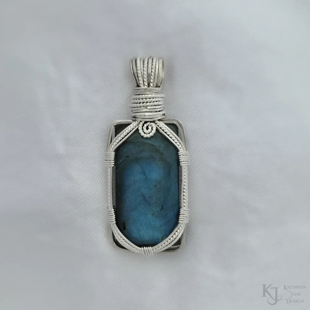 On this oblong-shaped labradorite, a secure but open support is provided by the sterling silver framework, with front design consisting of square wires either side of a central twisted silver strand. The top spiral provides decoration, as well as symbology for growth.