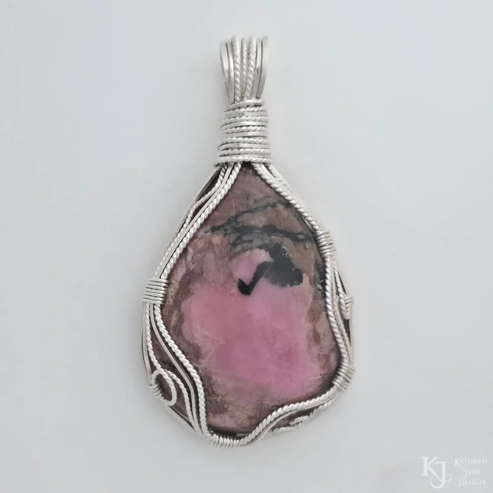Gentle curves of square and twisted silver frame this NZ rhodonite, bordering playful loops and spirals.