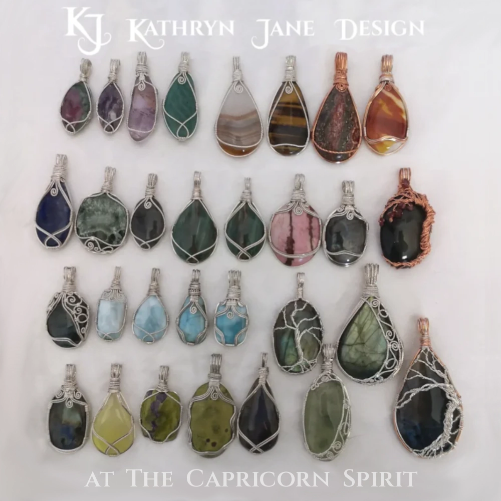 A selection of wire-wrapped crystal pendants on a white satin background. Many are sterling silver surrounding gemstones and crystals, with copper wire-wrapping also. Kathryn Jane Design pendants available at The Capricorn Spirit